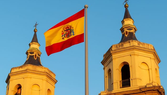 Bandeira da Espanha entre as torres de uma igreja (Foto: Folha Gospel/ Canva IA)